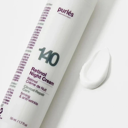 Na zdjęciu jest biała butelka produktu PURLES 140 Retinol Night Cream, leżąca na jasnym tle. Obok znajduje się próbka kremu w formie gładkiej, białej smugi, co pokazuje jego konsystencję – lekką i kremową. Na opakowaniu widoczny jest numer „140”.