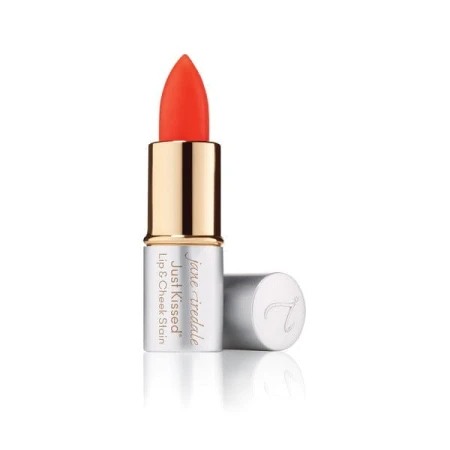 Na zdjęciu widoczna jest pomadka Just Kissed Lip and Cheek Stain forever red marki Jane Iredale. Produkt ma eleganckie opakowanie w odcieniach srebra i złota, z odkrytą szminką w soczystym czerwonym kolorze.