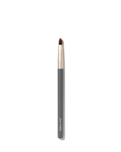 Na zdjęciu jest cienki pędzelek do makijażu jane iredale. Ma smukły kształt, szarą rączkę z logo marki i złotą skuwkę. Włosie pędzelka jest krótkie, ścięte w szpic, co sprawia, że idealnie nadaje się do precyzyjnej aplikacji produktów.