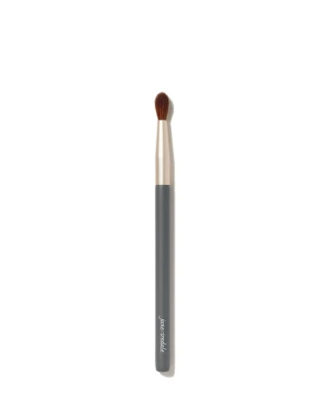 Na zdjęciu znajduje się pędzelek do oczu marki Jane Iredale. Ma elegancki, smukły trzonek w kolorze grafitu z napisem,  ściętą końcówkę z ciemnego włosia.  Pędzel jest przeznaczony do precyzyjnego nakładania cieni.