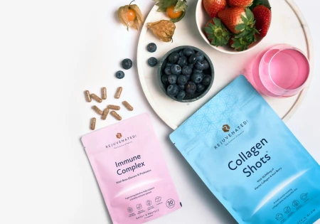 Na zdjęciu różowy suplement Immune Complex i niebieski Collagen Shots, świeże truskawki, borówki i napoje na tacy. Kompozycja promująca zdrowy styl życia i pielęgnację od wewnątrz.