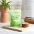 Zdjęcie przedstawia jasnozielone opakowanie suplementu Rejuvenated Skin Perfecting Complex, kapsułki w drewnianej misce, na drewnianej desce. W tle roślina doniczkowa i książka kucharska.