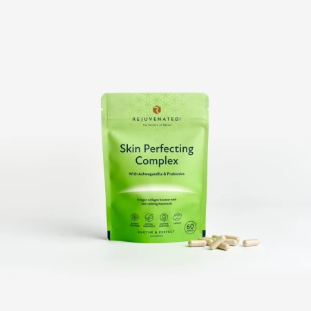 Zdjęcie przedstawia stojące, jasnozielone, zamykane strunowo opakowanie suplementu diety Rejuvenated Skin Perfecting Complex. Obok opakowania, na gładkim, jasnoszarym tle, rozsypanych jest kilka beżowych kapsułek.