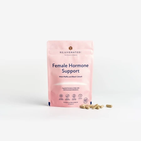 Na białym tle znajduje się różowa saszetka suplementu Rejuvenated Female Hormone Support. Przed opakowaniem leży kilka beżowych kapsułek. Na saszetce widnieje informacja o zawartości pfafii i pluskwicy groniastej (Black Cohosh)