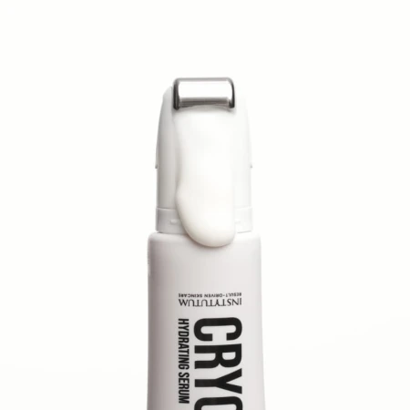 Na zdjęciu znajduje się kosmetyk marki Instytutum – serum nawilżające CRYO SHOT HYDRATING SERUM. Produkt znajduje się w białym opakowaniu z aplikatorem zakończonym metalową kulką chłodzącą, z którego wypływa kremowa formuła.