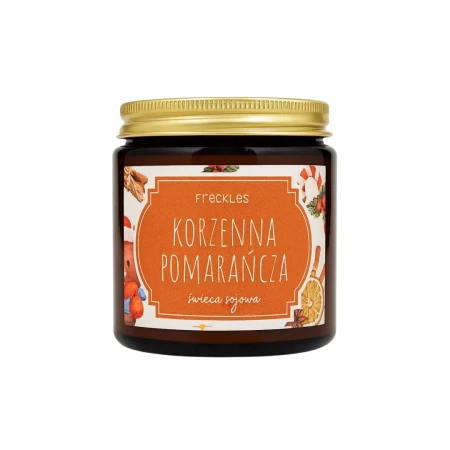 Na zdjęciu znajduje się świeca sojowa marki Freckles o nazwie Korzenna Pomarańcza. Produkt umieszczony jest w szklanym słoiczku z metalową, złotą zakrętką. Etykieta w odcieniu pomarańczowym ozdobiona jest świątecznymi grafikami przypraw