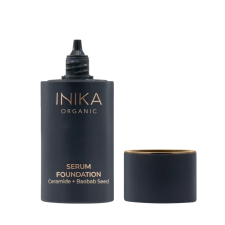 Na zdjęciu widoczny jest otwarty produkt marki INIKA Organic – Serum Foundation z ceramidami i nasionami baobabu. Ciemnogranatowe, matowe opakowanie o eleganckim wyglądzie posiada złote akcenty w postaci logotypu i nazwy produktu.