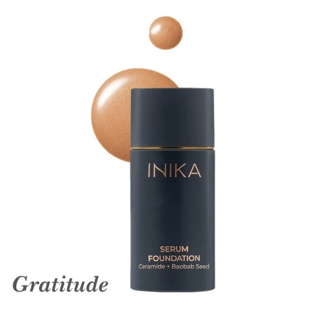 Na zdjęciu widoczny jest podkład INIKA Organic Serum Foundation w odcieniu Gratitude. Produkt znajduje się w granatowej butelce z eleganckim złotym napisem, a obok jest próbka koloru – ciepły, głęboki odcień brązu z delikatnym, świetlistym wykończeniem.