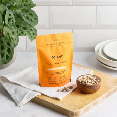 Zdjęcie przedstawia stojące, pomarańczowe opakowanie suplementu diety w kapsułkach Rejuvenated Re-set. Produkt jest opisany jako naturalny suplement diety wspierający zdrowy metabolizm komórkowy, energię i spalanie tłuszczu.