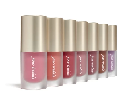 Na zdjęciu widać kilka błyszczyków do ust ustawionych obok siebie. Opakowania są przezroczyste, z jasnymi, złotymi nakrętkami, a kolory produktów przechodzą od jasnego nude przez różne odcienie różu po głębsze, bardziej nasycone tony.
