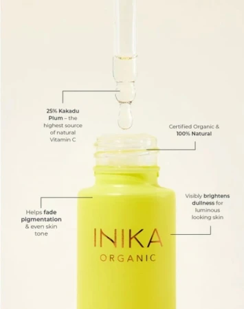 Na zdjęciu znajduje się buteleczka serum INIKA Organic Kakadu Plum Vitamin C Booster w charakterystycznym żółtym kolorze, z przezroczystą pipetą unoszącą się nad otwartą szyjką opakowania. Z pipety spada kropla serum