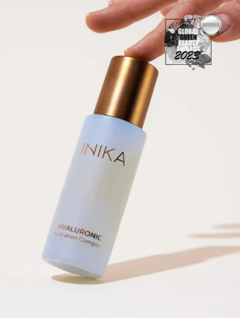 Na zdjęciu widoczny jest kosmetyk marki INIKA Organic – Hyaluronic Hydration Complex, trzymany delikatnie dwoma palcami.