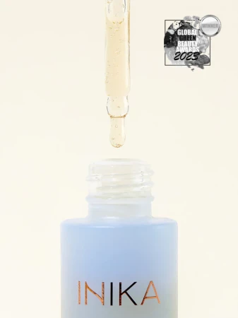 Na zdjęciu znajduje się buteleczka serum INIKA Organic Hyaluronic Hydration Complex w eleganckim, matowym, błękitnym odcieniu. Z pipety widocznej nad otwartą butelką wypływa przejrzysty płyn, co sugeruje lekką, nawilżającą formułę produktu.