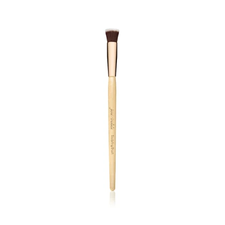 Na zdjęciu Sculpting Brush marki Jane Iredale, krótki, płaski, ścięty pod kątem, do konturowania  Rączka drewniana z jasnego drewna, złota skuwka, nadrukowana nazwa marki i pędzla  Włosie syntetyczne, zbite, w kolorze ciemnobrązowym z jasnymi końcówkami