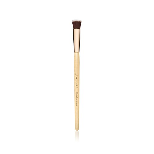 Na zdjęciu Sculpting Brush marki Jane Iredale, krótki, płaski, ścięty pod kątem, do konturowania  Rączka drewniana z jasnego drewna, złota skuwka, nadrukowana nazwa marki i pędzla  Włosie syntetyczne, zbite, w kolorze ciemnobrązowym z jasnymi końcówkami