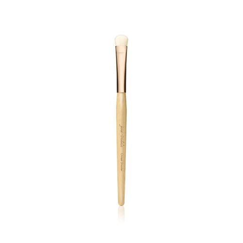 Na zdjęciu widoczny jest pędzel do makijażu marki Jane Iredale. Jest to cienki, precyzyjny pędzel o długim, drewnianym trzonku w naturalnym kolorze, z elegancką, złotą skuwką. Główka pędzla jest mała, zaokrąglona, wykonana z jasnego włosia.