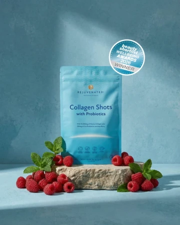Niebieskie opakowanie Collagen Shots with Probiotics marki Rejuvenated na turkusowym tle. Stoi na kamieniu, obok maliny i mięta. Widoczna plakietka nagrody Beauty Wellbeing Awards 2026 Winner.jpg