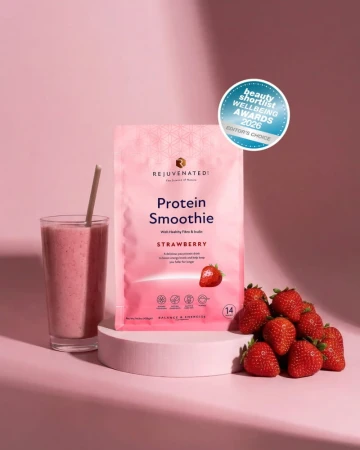 Różowe opakowanie Protein Smoothie Strawberry marki Rejuvenated na tle w kolorze pudrowego różu, obok szklanka koktajlu i świeże truskawki. Widoczna plakietka nagrody 2026 Editors Choice.jpg