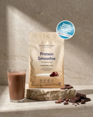 Beżowe opakowanie odżywki Protein Smoothie Chocolate marki Rejuvenated, obok szklanka napoju czekoladowego i kawałki czekolady; widoczne oznaczenie nagrody Beauty Shortlist Wellbeing Awards 2026 – Editor’s Choice.jpg