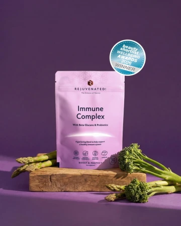 Lawendowe opakowanie Immune Complex marki Rejuvenated na fioletowym tle, stoi na drewnianej podstawie. Obok zielone warzywa i oznaczenie nagrody Beauty Wellbeing Awards 2026 Winner.jpg