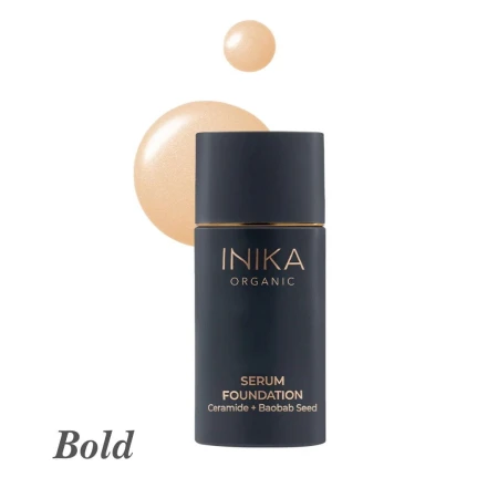 Na zdjęciu przedstawiono odcień Bold z gamy INIKA Organic Serum Foundation. Produkt znajduje się w eleganckiej buteleczce w matowym, granatowym kolorze ze złotymi akcentami. Obok opakowania widoczna jest próbka koloru