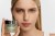 Modelka trzyma w dłoni słoiczek Instytutum Superbiotic Regeneration Cream. Krem przedstawiony jest w eleganckim, matowym opakowaniu z metaliczną nakrętką. Ujęcie podkreśla efekt zdrowej, gładkiej i promiennej skóry