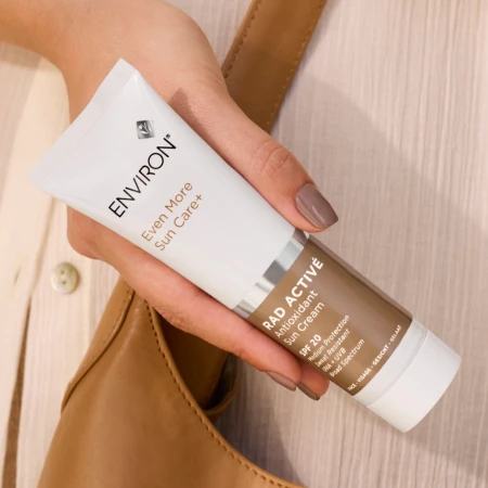 Dłoń trzyma produkt marki Environ RAD ACTIVÉ Antioxidant Sun Cream SPF 20. Ujęcie lifestyle’owe podkreśla wakacyjny charakter pielęgnacji przeciwsłonecznej i elegancki, minimalistyczny design.png