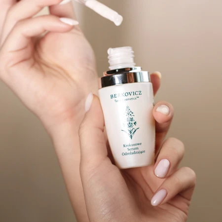 Zbliżenie na aplikację Berkovicz Tatra Cosmetics – Krokusowe Serum Odmładzające trzymane w dłoni. Pipeta z delikatną kroplą serum unosi się nad otwartą butelką z eleganckim, srebrnym wykończeniem.