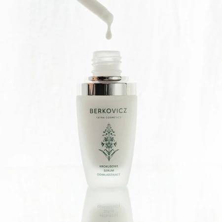 Artystyczne ujęcie Berkovicz Tatra Cosmetics – Krokusowe Serum Odmładzające w trakcie aplikacji. Nad otwartą butelką z eleganckim, srebrnym wykończeniem unosi się kropla serum spływająca z pipety