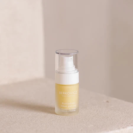 Na zdjęciu widoczny jest Rumiankowy Eliksir pod oczy Berkovicz Tatra Cosmetics ustawiony na jasnym, naturalnym tle. Szklana butelka z pompką i przezroczystą nakładką ochronną eksponuje złocistą formułę produktu.