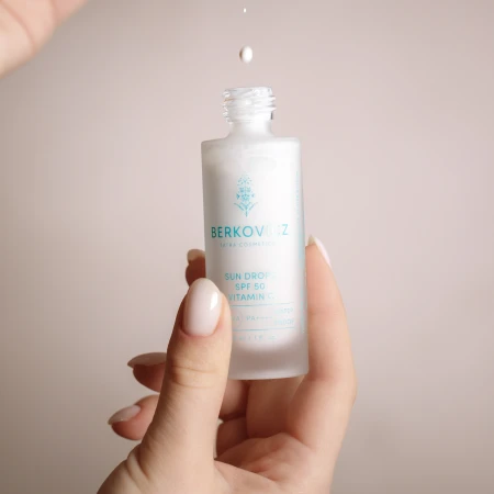 Minimalistyczne ujęcie produktu Berkovicz Tatra Cosmetics – Sun Drops SPF 50 Witamina C z kroplą serum unoszącą się nad butelką. Delikatna, lekka konsystencja podkreśla nowoczesną formułę z wysoką ochroną UVA/UVB oraz pielęgnacyjnym działaniem witaminy C