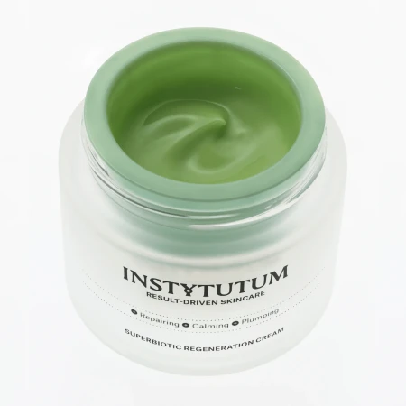 Zbliżenie na otwarty słoik Instytutum Superbiotic Regeneration Cream. Wnętrze wypełnia krem o charakterystycznym, świeżym zielonym kolorze i jedwabistej, gładkiej konsystencji z delikatnym wirującym wykończeniem.