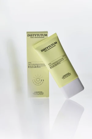 Na zdjęciu widać opakowanie i tubę kremu przeciwsłonecznego INSTYTUTUM Sunscription Dark Spot Defence SPF 50 w jasnozielonym kolorze, ustawione na jasnym tle z delikatnym odbiciem produktu.