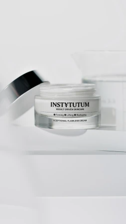 Na zdjęciu widać otwarty słoiczek kremu INSTYTUTUM Xceptional Flawless Cream z odłożoną srebrną zakrętką, ustawiony na jasnym, minimalistycznym tle.