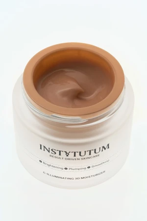 Na zdjęciu widać otwarty słoiczek kremu INSTYTUTUM C-Illuminating 3D Moisturizer z widoczną, kremową formułą w odcieniu ciepłego beżu.