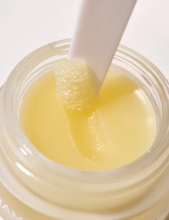 Na zdjęciu widoczne jest zbliżenie na balsam do ust INIKA Organic w słoiczku, z aplikatorem zanurzonym w gładkiej, odżywczej formule, podkreślającym jego bogatą i jedwabistą konsystencję.
