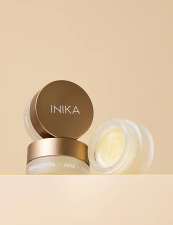Na zdjęciu widoczne są otwarte słoiczki maski do ust INIKA Organic Lip Mask Bakuchiol + AHA, prezentujące odżywczą formułę wzbogaconą bakuchiolem, kwasami AHA i ceramidami na eleganckim, beżowym tle.
