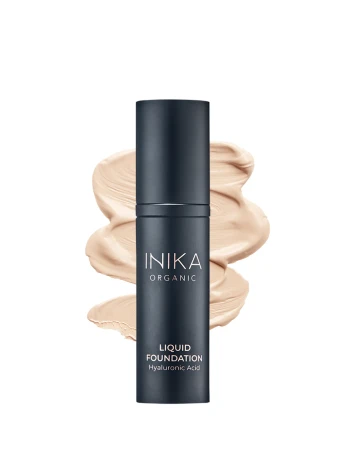 Na zdjęciu widoczny jest podkład INIKA Organic Liquid Foundation z kwasem hialuronowym w eleganckim, ciemnym opakowaniu, zaprezentowany na tle rozprowadzonego produktu, który podkreśla jego kremową konsystencję i naturalne wykończenie makijażu.