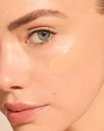 Zdjęcie typu „przed i po” przedstawia zbliżenie twarzy modelki. Po lewej skóra jest naturalna, a po prawej po aplikacji produktu wygląda na bardziej wyrównaną, wygładzoną i wyraźnie rozświetloną.