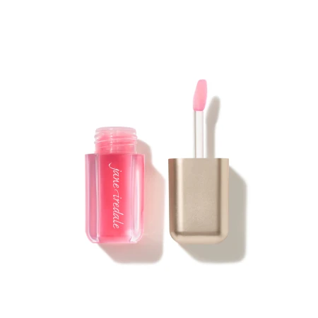 Na białym tle jest otwarty olejek do ust Jane Iredale Just Kissed Lip Oil w przezroczystym opakowaniu, w intensywnym różowym odcieniu. Obok znajduje się złota nakrętka z wysuniętym aplikatorem o miękkiej, zaokrąglonej końcówce pokrytej różowym olejkiem.