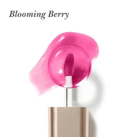Na białym tle jest aplikator olejku do ust Jane Iredale Just Kissed Lip Oil z miękką, zaokrągloną końcówką w intensywnym różowo jagodowym kolorze. W tle widoczna jest rozsmarowana próbka olejku o transparentnej, błyszczącej konsystencji i odcieniu fuksji.
