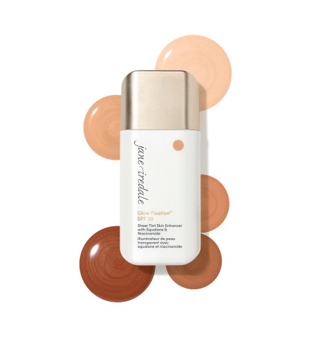 Na zdjęciu widać Jane Iredale Glow Fixation SPF 30 Sheer Tint Skin Enhancer w białym opakowaniu z aplikatorem. Wokół produktu pokazano próbki kosmetyku w kilku tonacjach – od jasnych beżowo-brzoskwiniowych po głębsze, ciepłe brązy.